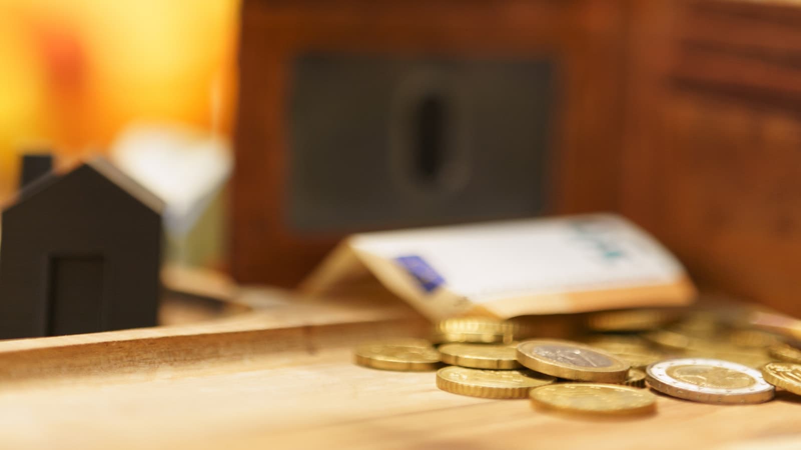 A small black house-shaped figurine on a table beside coins and a blurred wallet