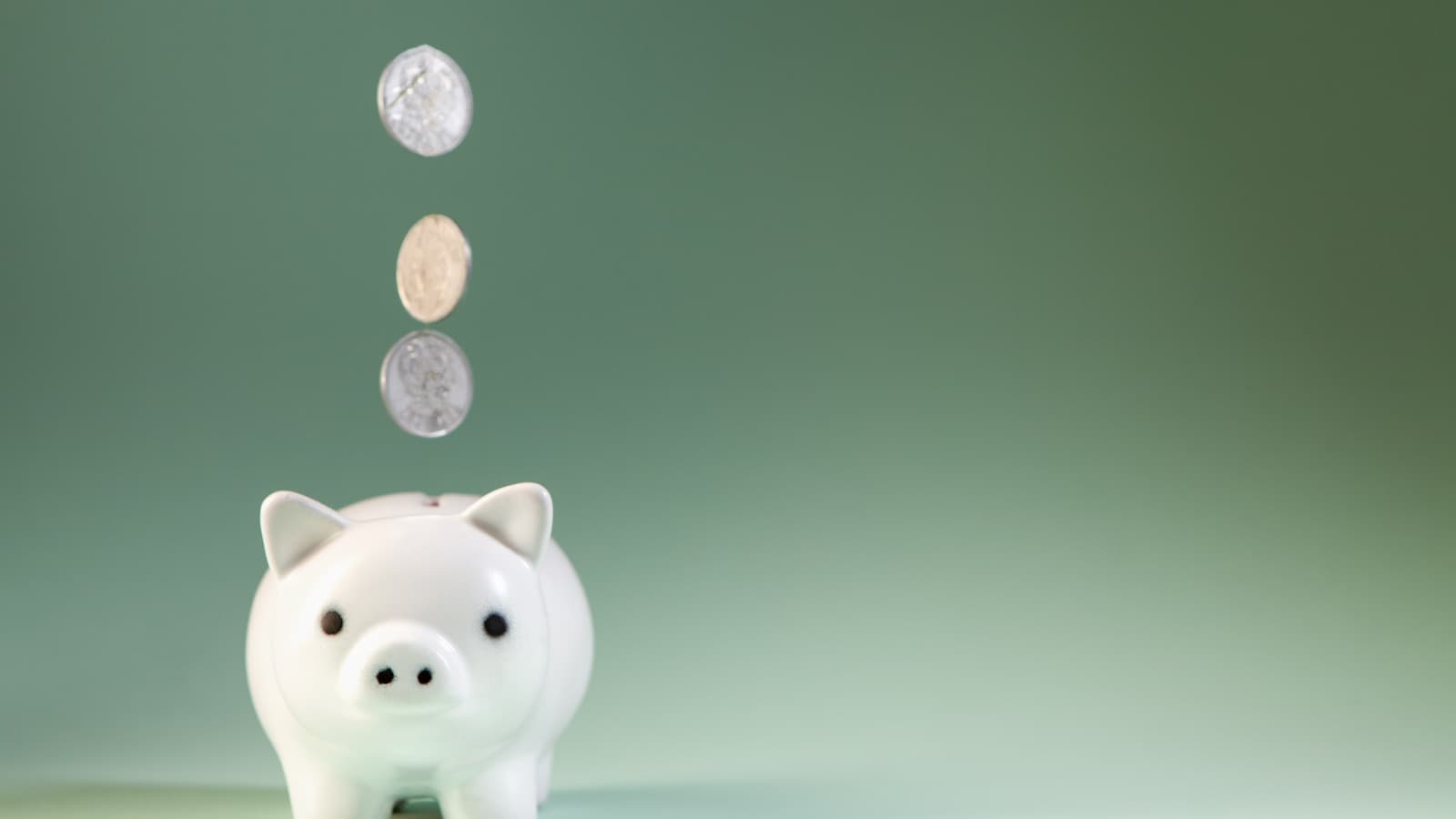 Coins falling into a white piggy bank against a modern green gradient background.