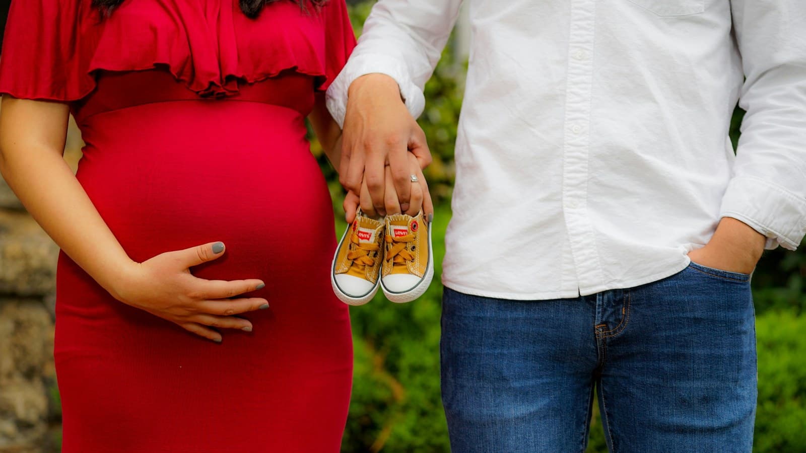 An expecting couple holding a small pair of baby shoes together.