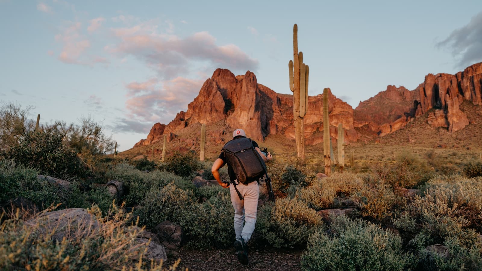 A hiker with a backpack on a desert trail toward mountains at golden hour.