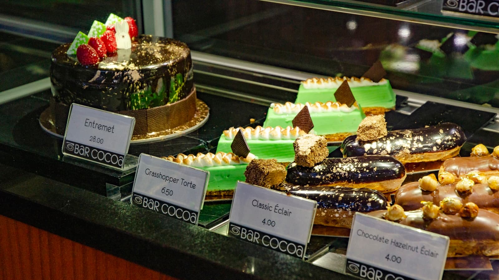 A bakery display case filled with colorful French-style cakes, pastries, and eclairs.