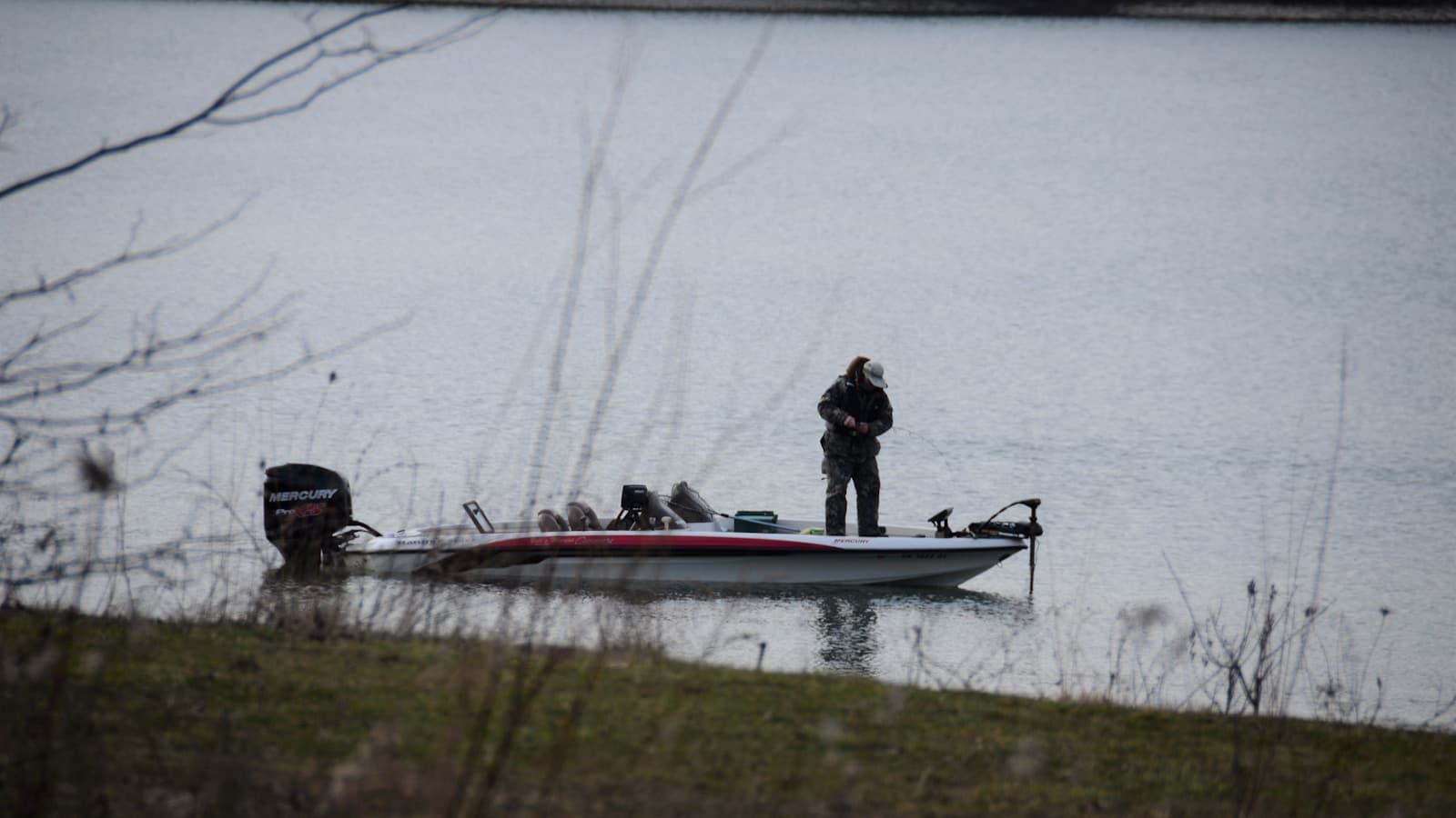 A person in a red-and-white bass boat on a lake during daylight.