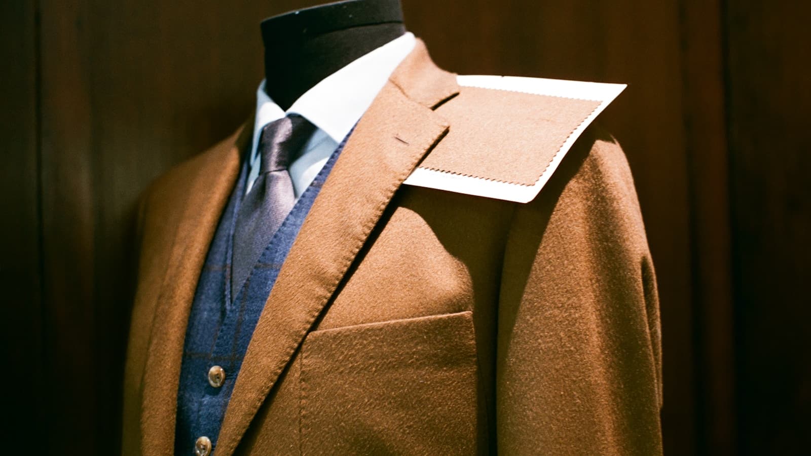 A brown tailored jacket displayed on a mannequin with a fabric swatch pinned to the shoulder.