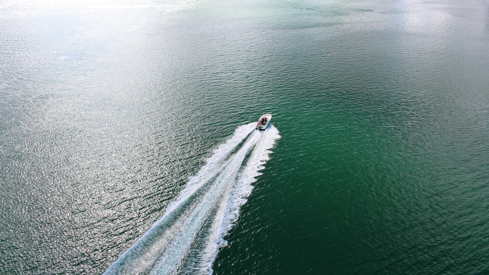 Aerial shot of a small speedboat cutting a white wake across turquoise water, occupants too distant to be identifiable.