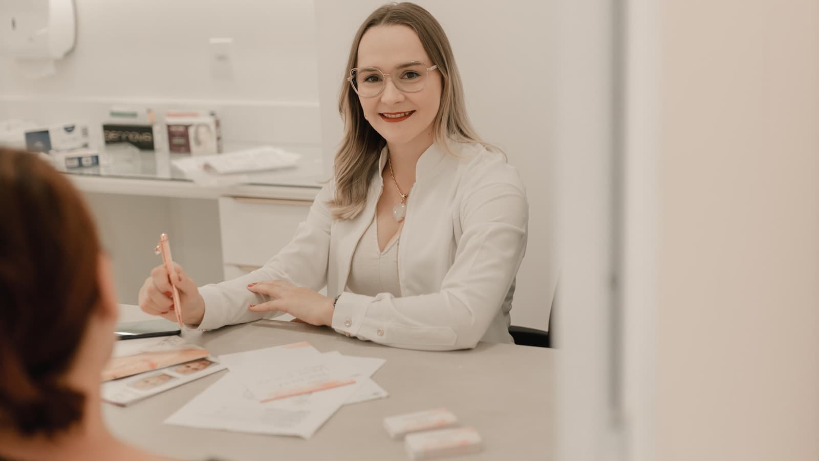 A woman smiling in consultation across a glass table from a professional, modern clinic.