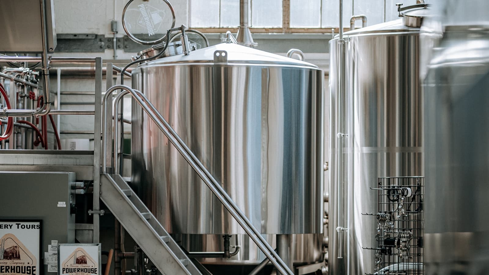 A large industrial room filled with rows of stainless steel brewing tanks.