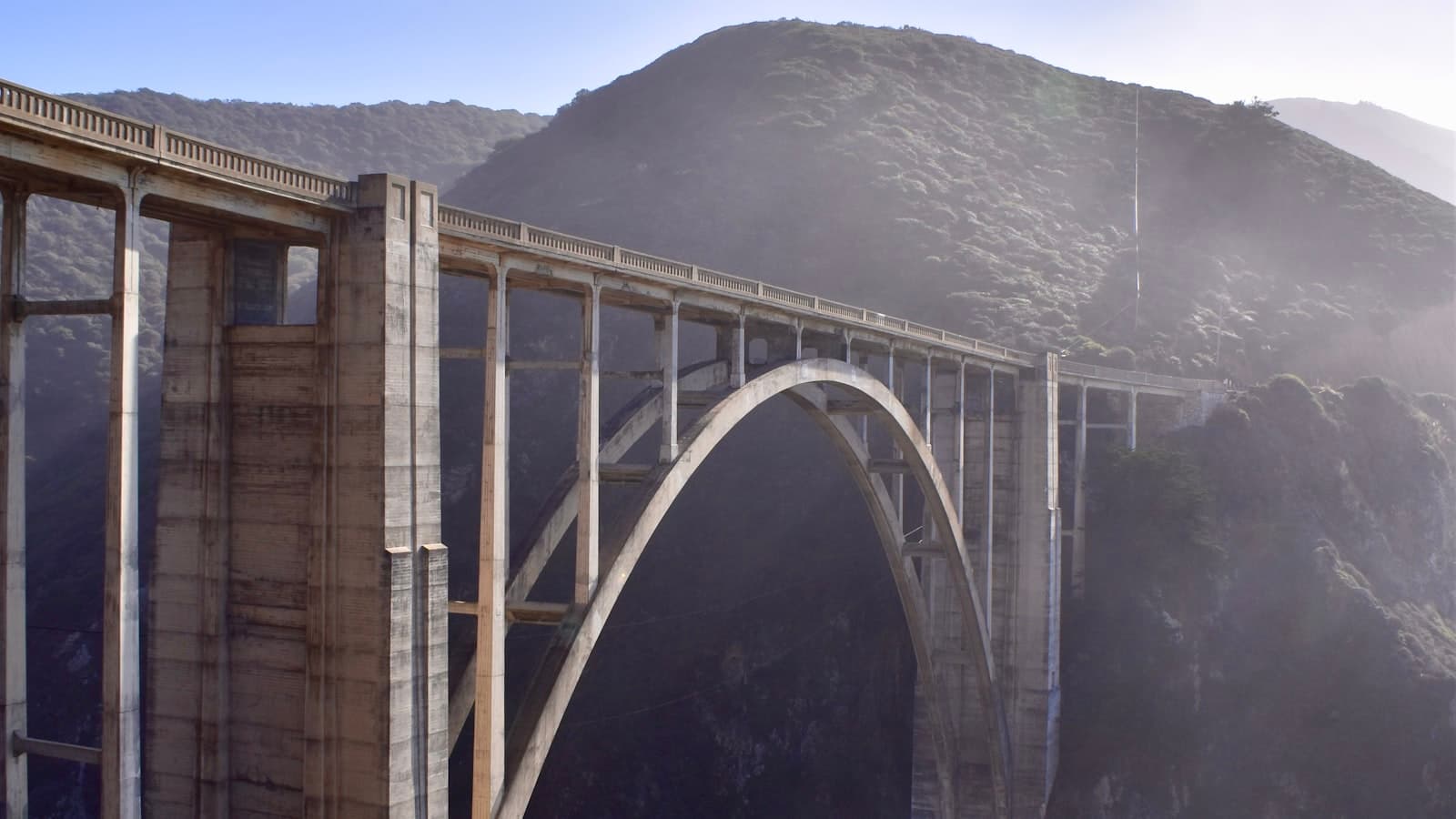 A tall concrete arch bridge spanning a misty coastal canyon, used as a visual metaphor for a bridge loan, with no people, text, or logos.