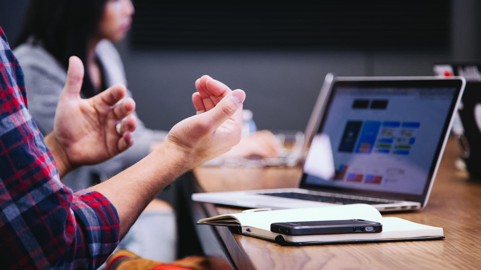A person gesturing while explaining a chart on a laptop screen to a colleague.