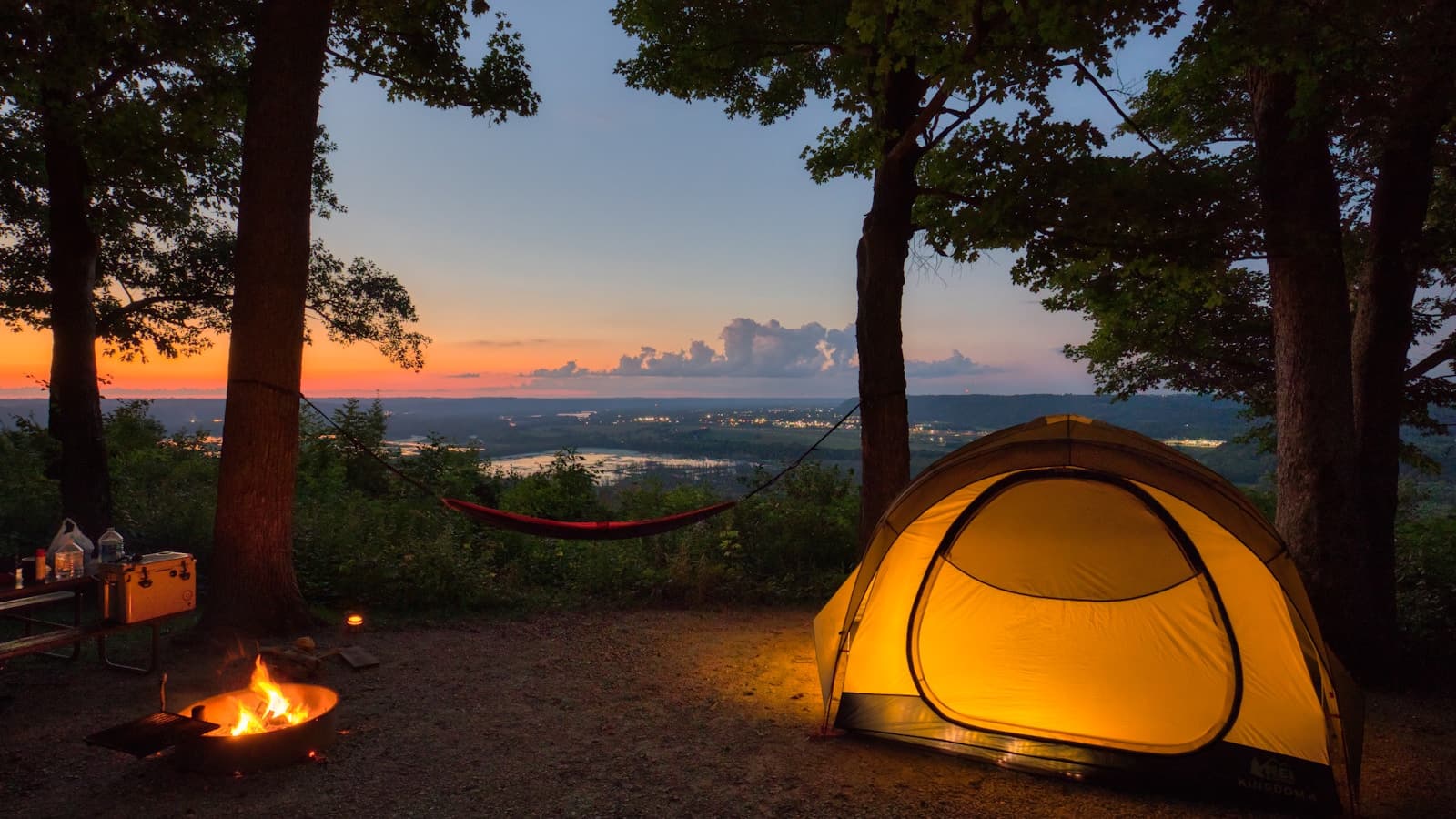 A tent set up in the woods during a golden sunset.