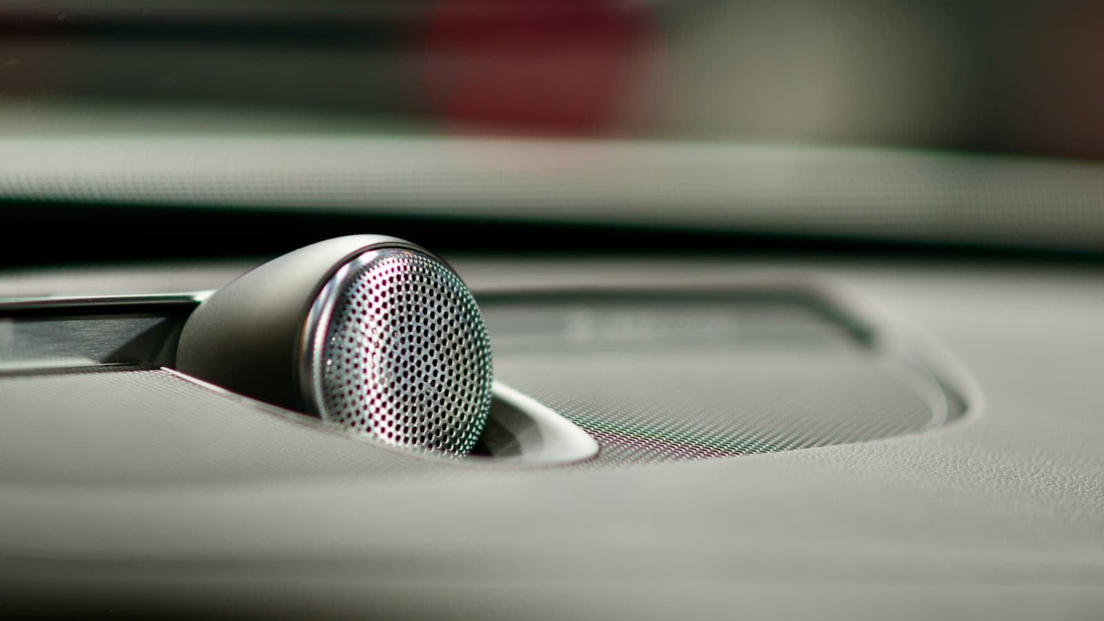 Close-up of a tweeter speaker mounted in a car dashboard with a modern silver mesh grille.