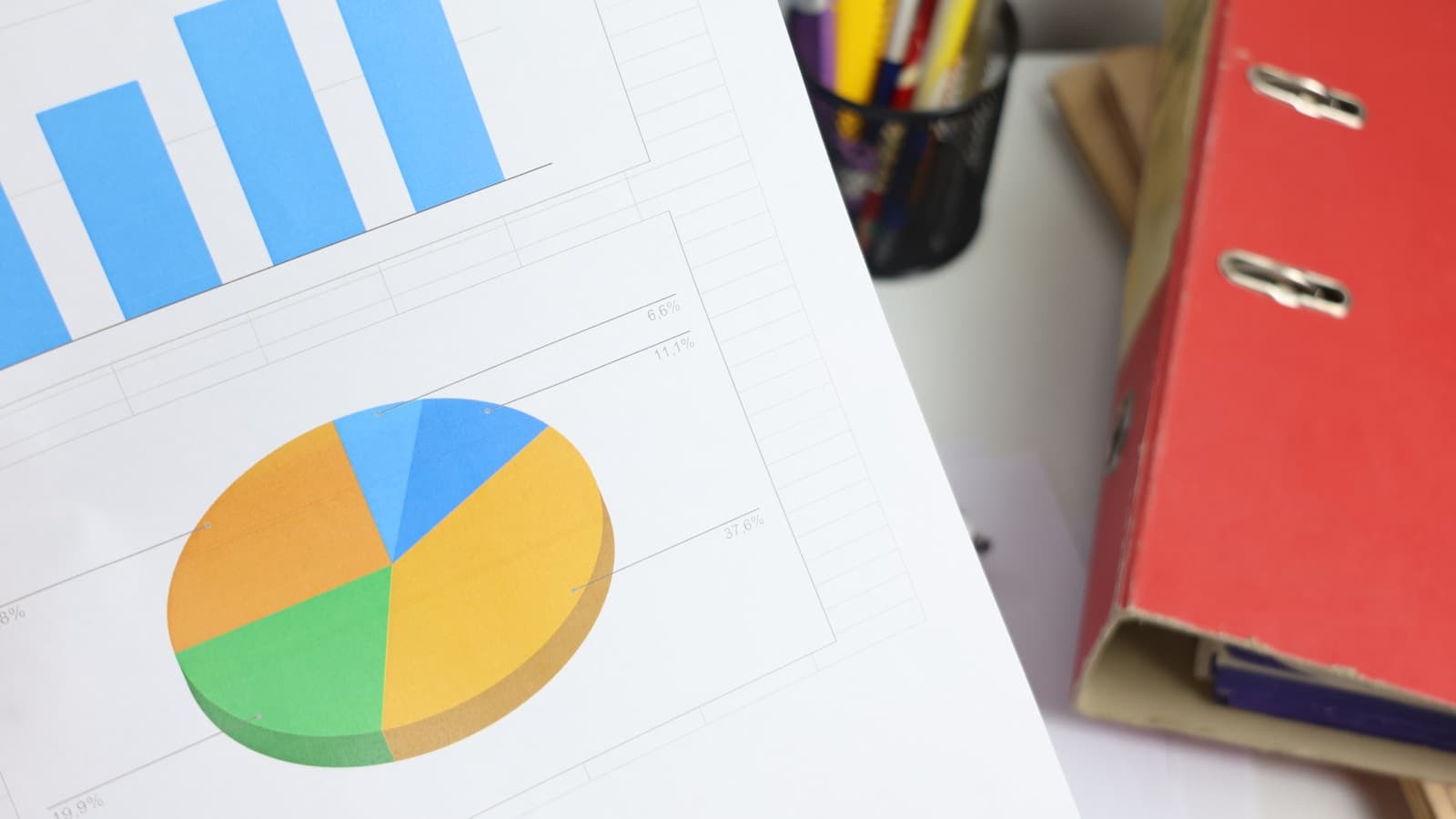 Bar and pie charts on a printed document next to a pen cup and binder.