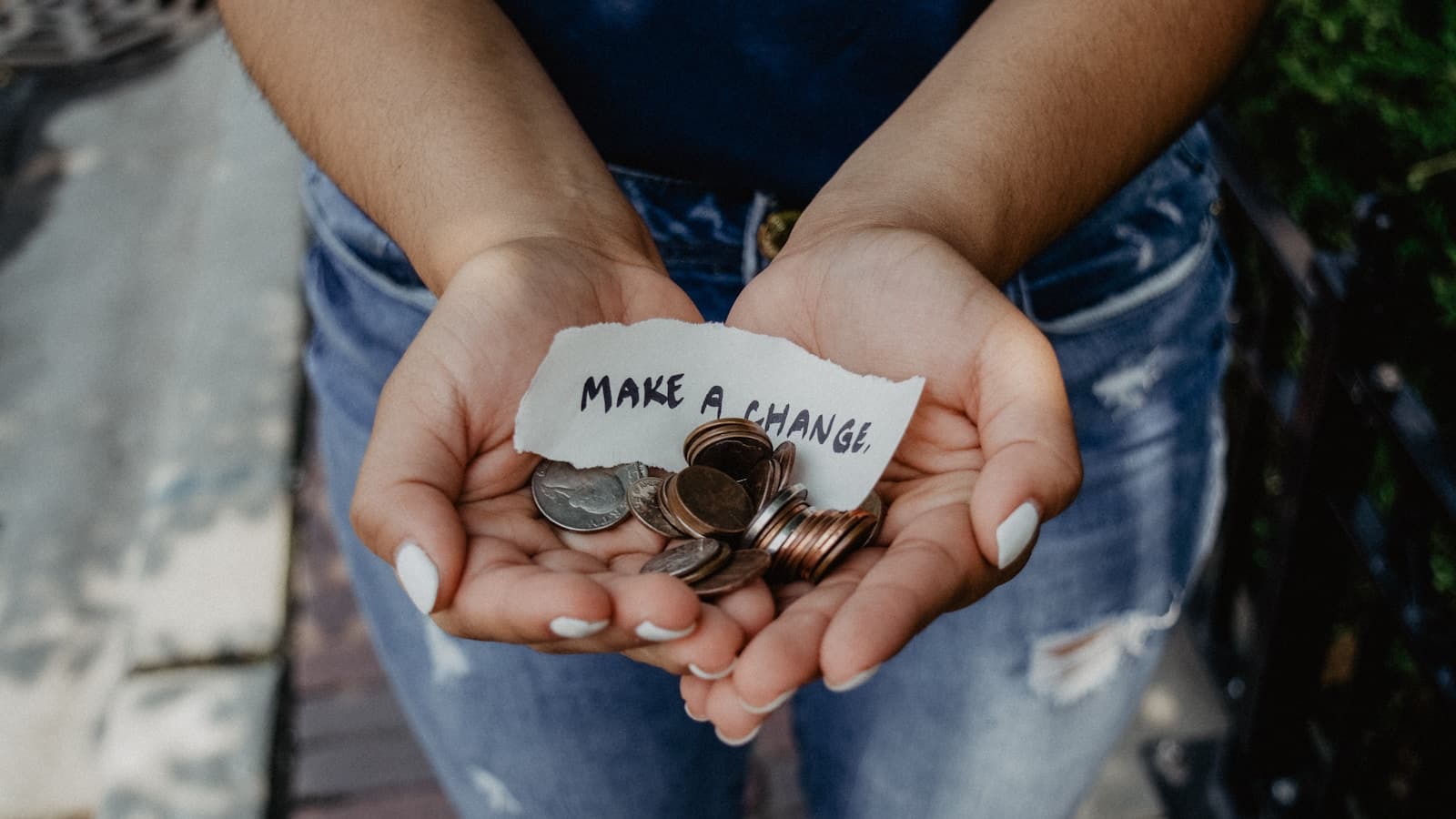Cupped hands holding coins and a handwritten note, generic charitable-giving image.