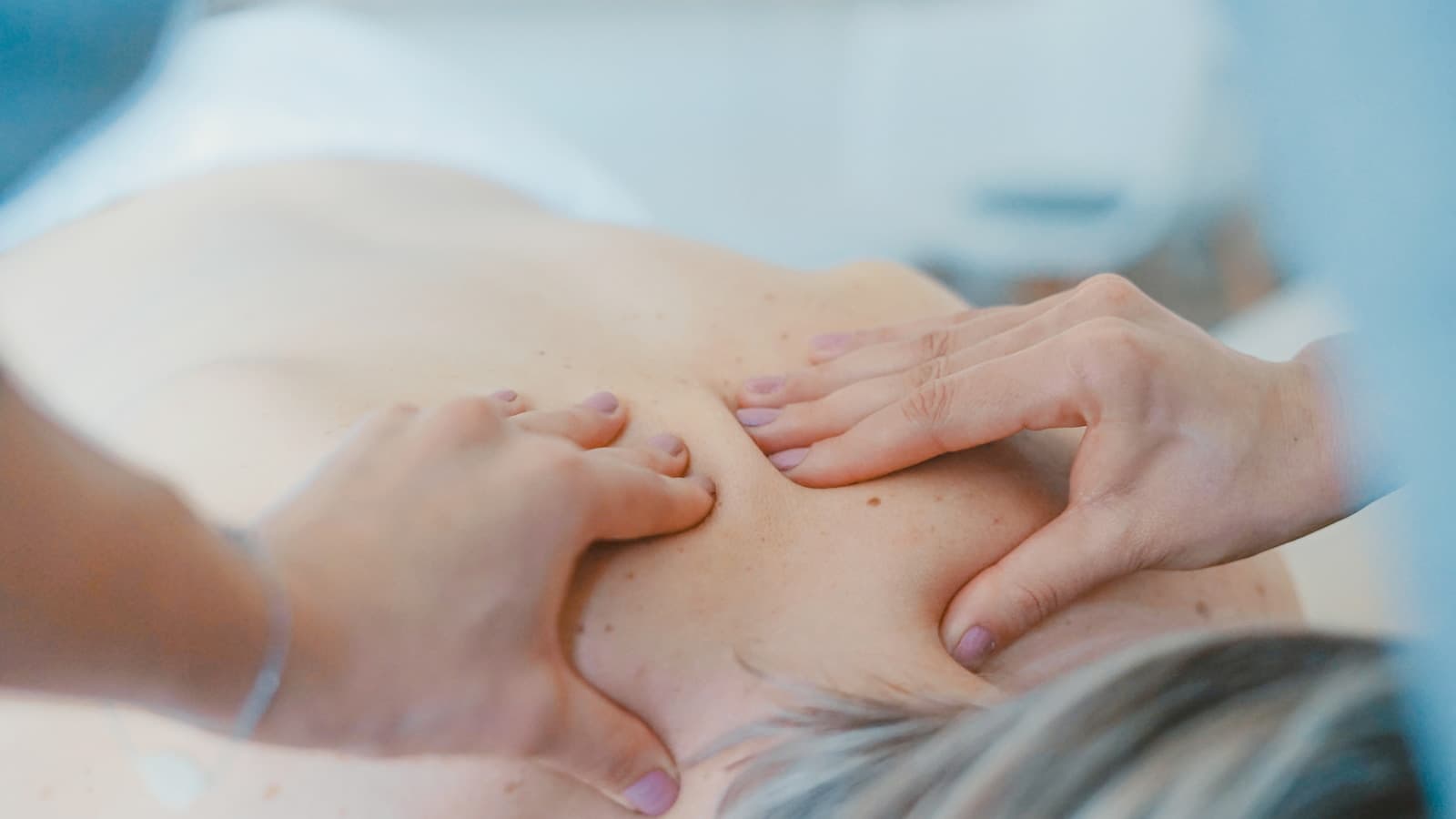 Close-up of hands treating a patient's upper back and shoulder area.