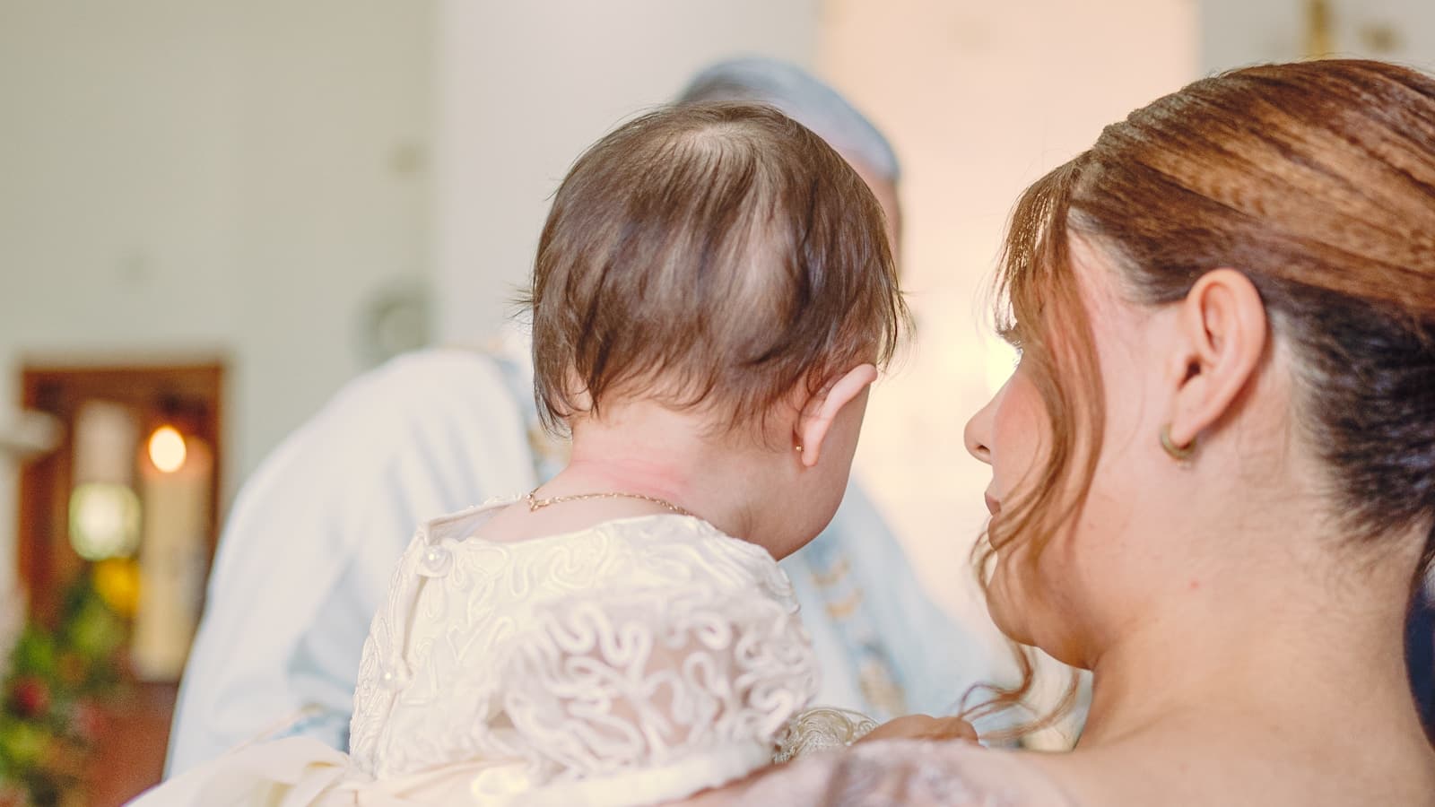 A mother holding her baby during a quiet ceremony, soft candlelit background.