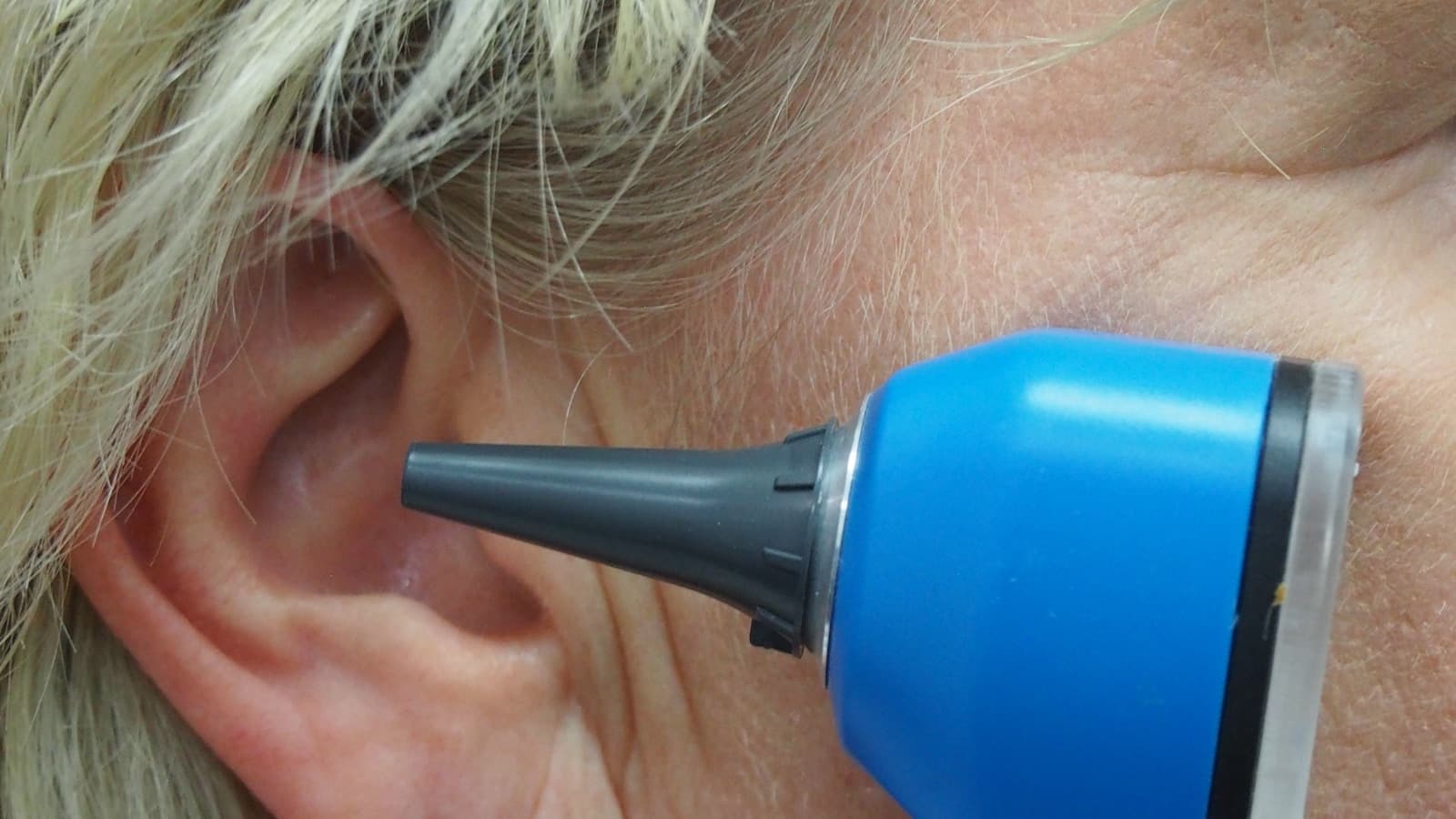 A dignified close-up of a doctor using an otoscope to examine a woman's ear.