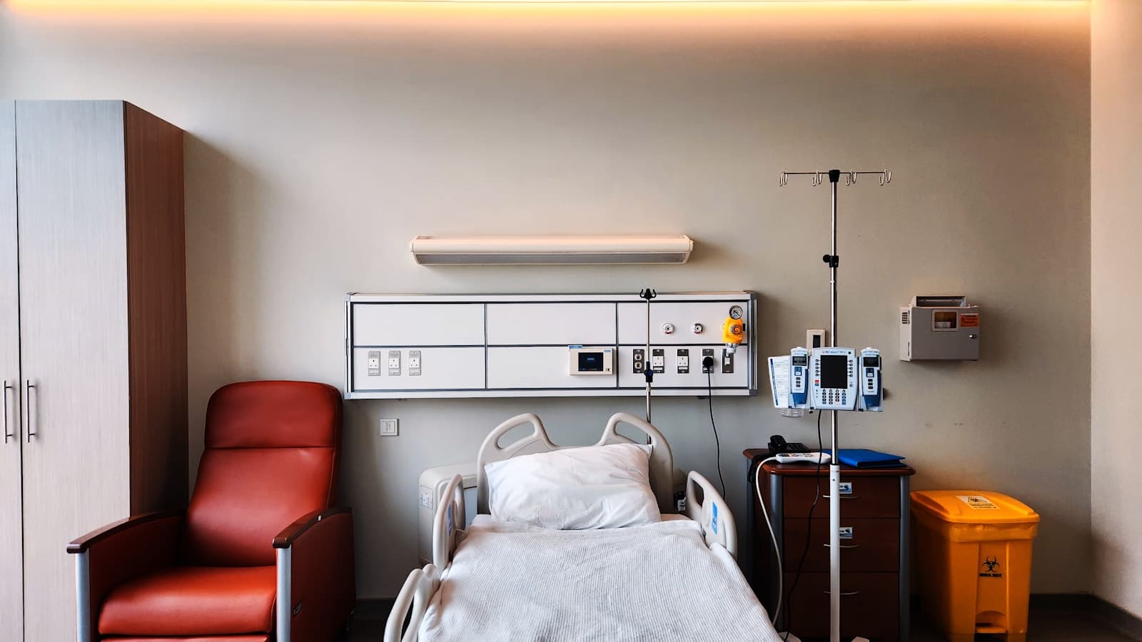 A calm, modern hospital room with a made bed, recliner chair, and monitoring equipment.