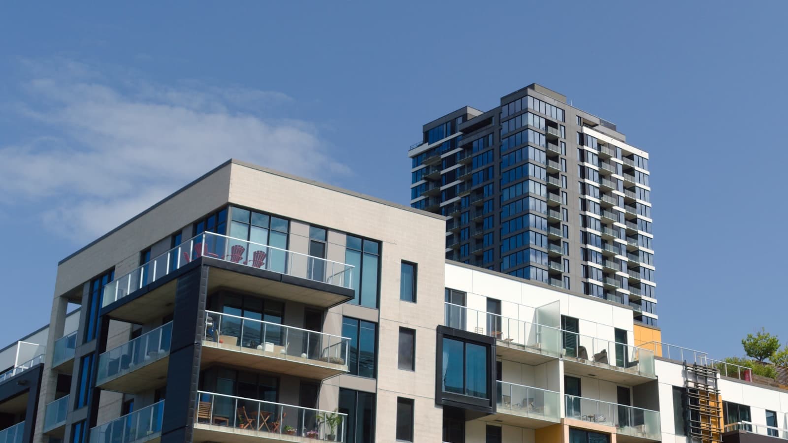 Two modern high-rise residential condo towers with glass balconies photographed from below against a clear blue sky.