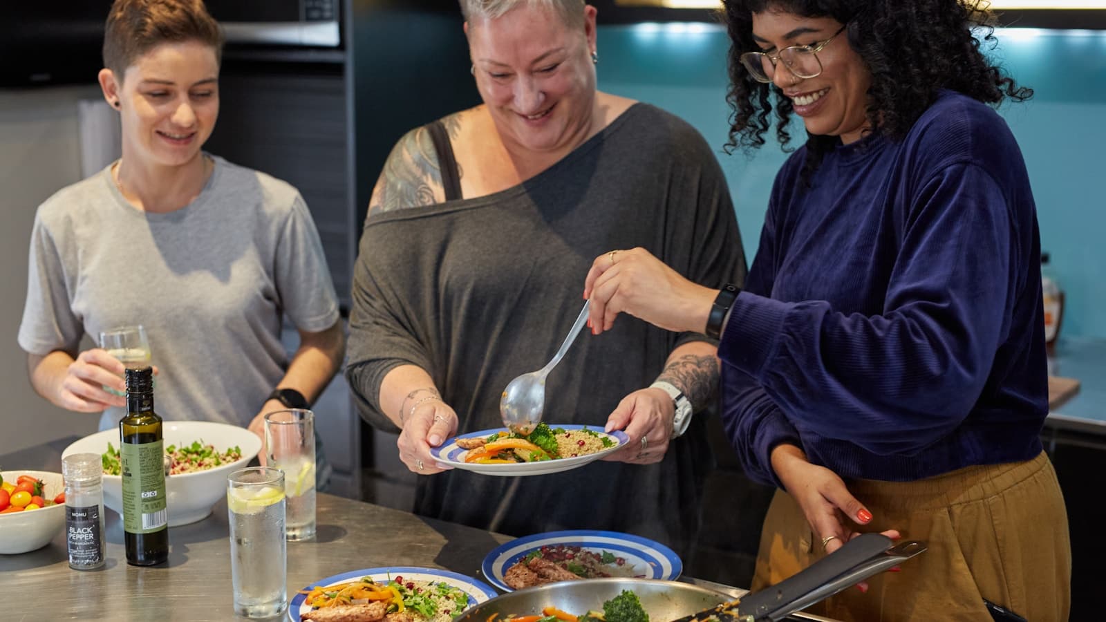 Three people gathered around a kitchen island together, plating a home-cooked meal.