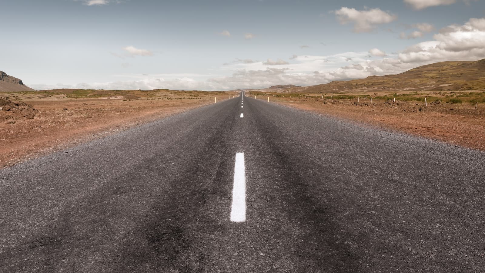 An empty two-lane highway stretching straight to the horizon through a mountainous landscape, symbolizing a long-distance move, with no people or vehicles visible.