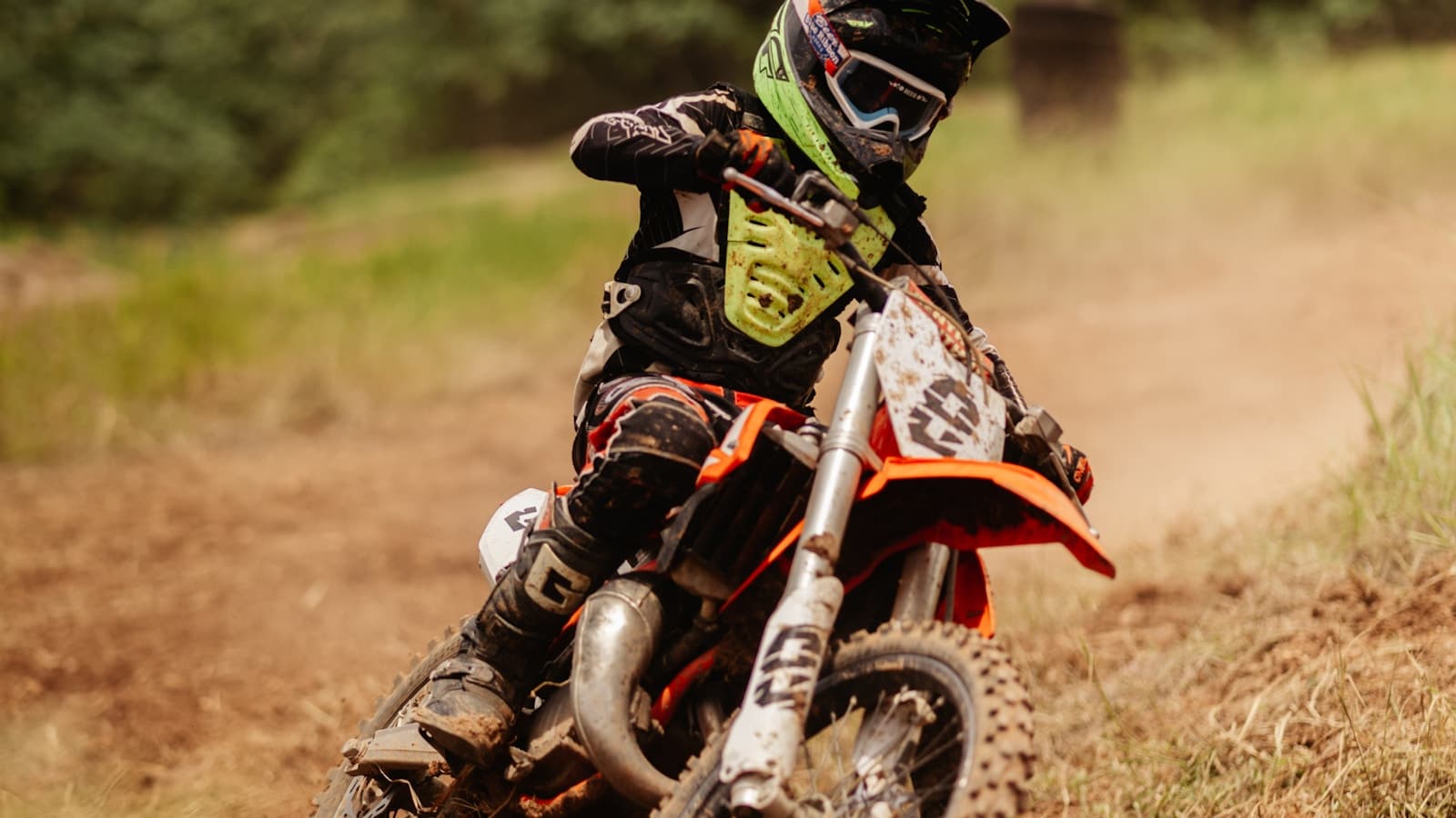 A young rider on a dirt bike navigating a dusty trail in full protective gear.