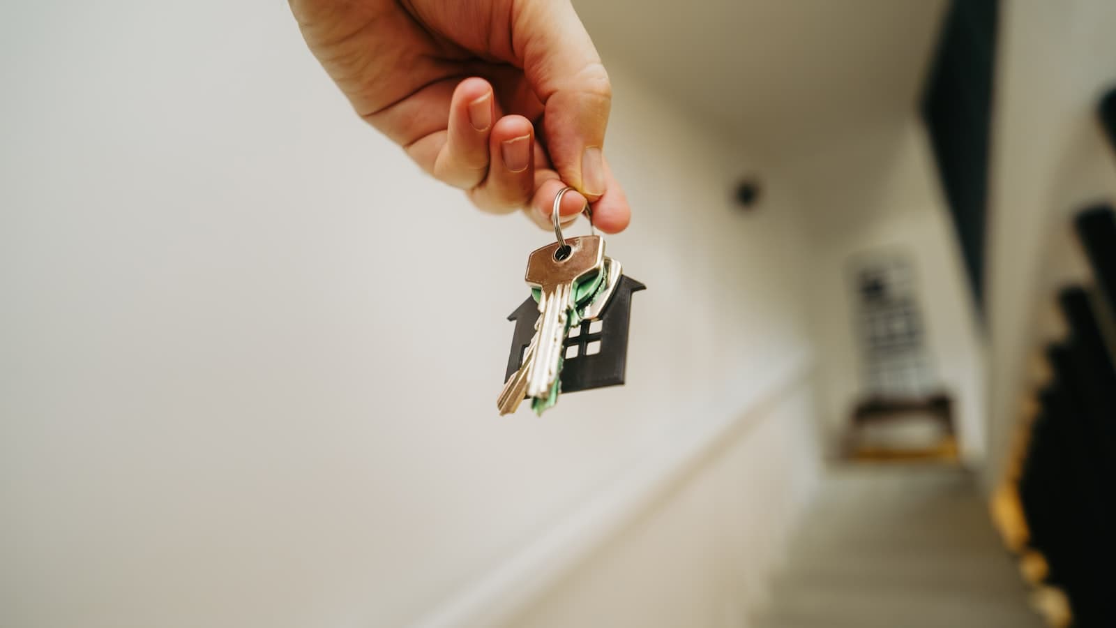 A hand holding a house-shaped keychain with keys in a bright hallway, symbolizing receiving keys after a home purchase, with no visible face or readable text.
