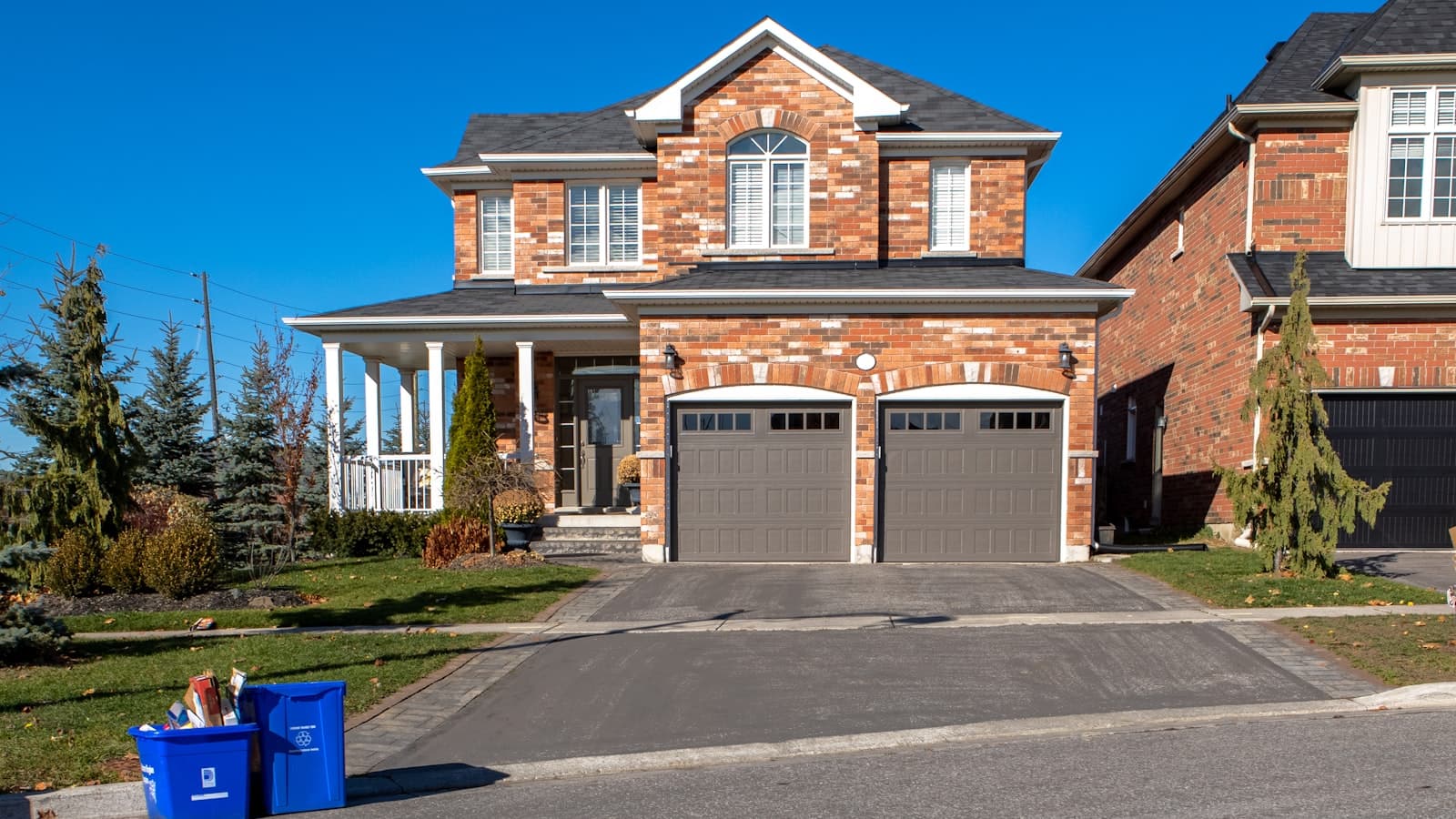 A brick two-story house with a clean paved driveway leading to its double garage; no faces, plates, or readable text visible.