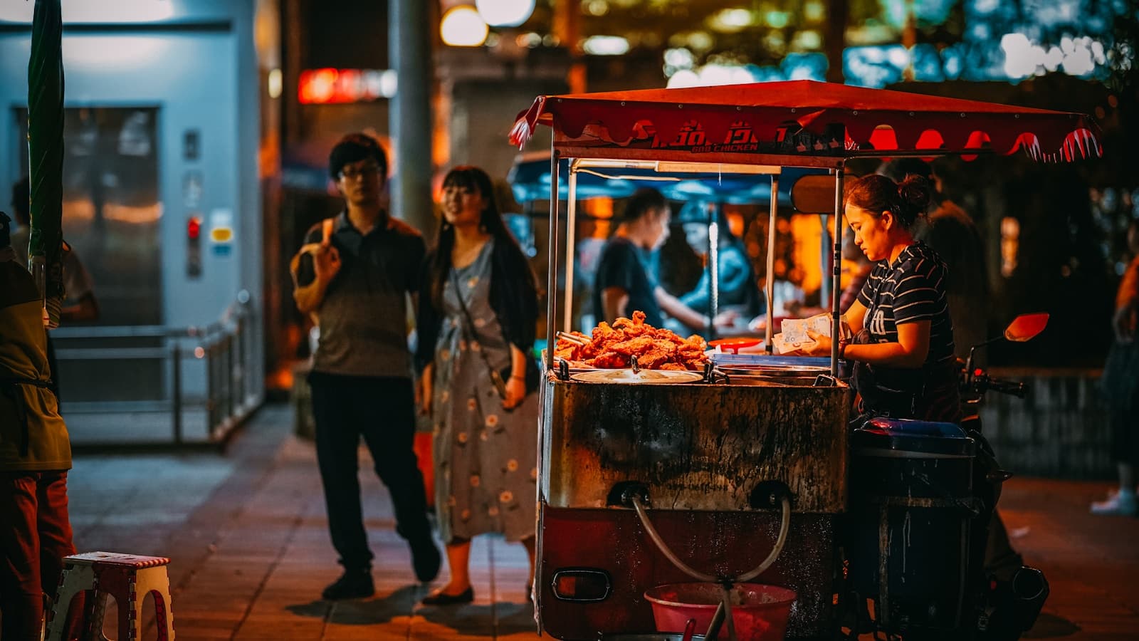 A nighttime street food cart with a vendor serving customers, warm bokeh lighting.