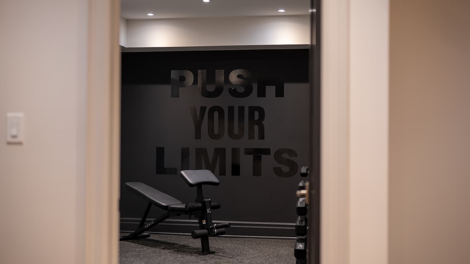 A dark-painted home gym room with a workout bench and dumbbells.