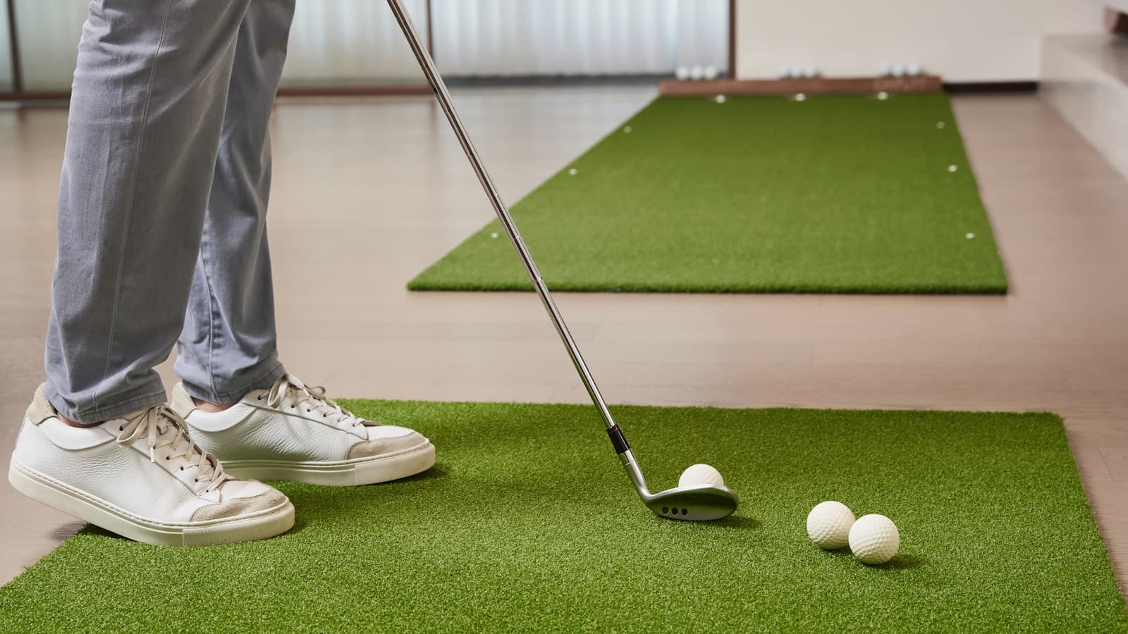 A person practicing a chip shot on an indoor golf mat in a modern living room.