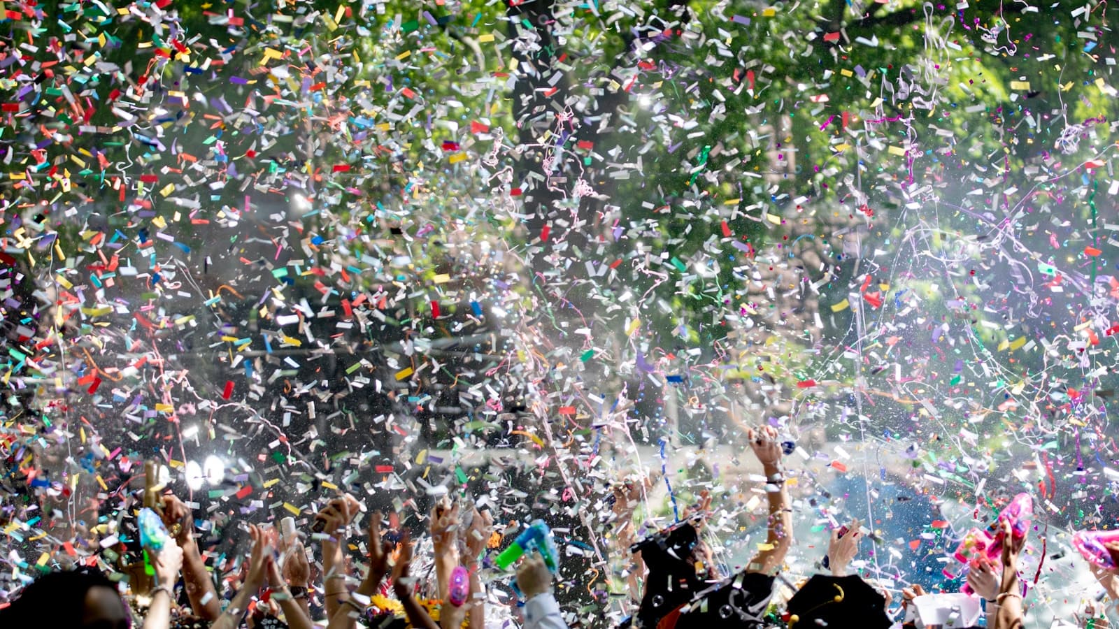 A crowd of graduates in caps and gowns celebrating under a shower of confetti outdoors.