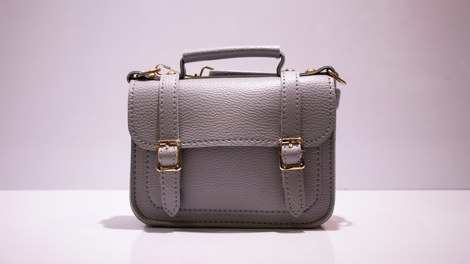 A plain gray leather satchel handbag with gold buckles on a white background; no visible branding.