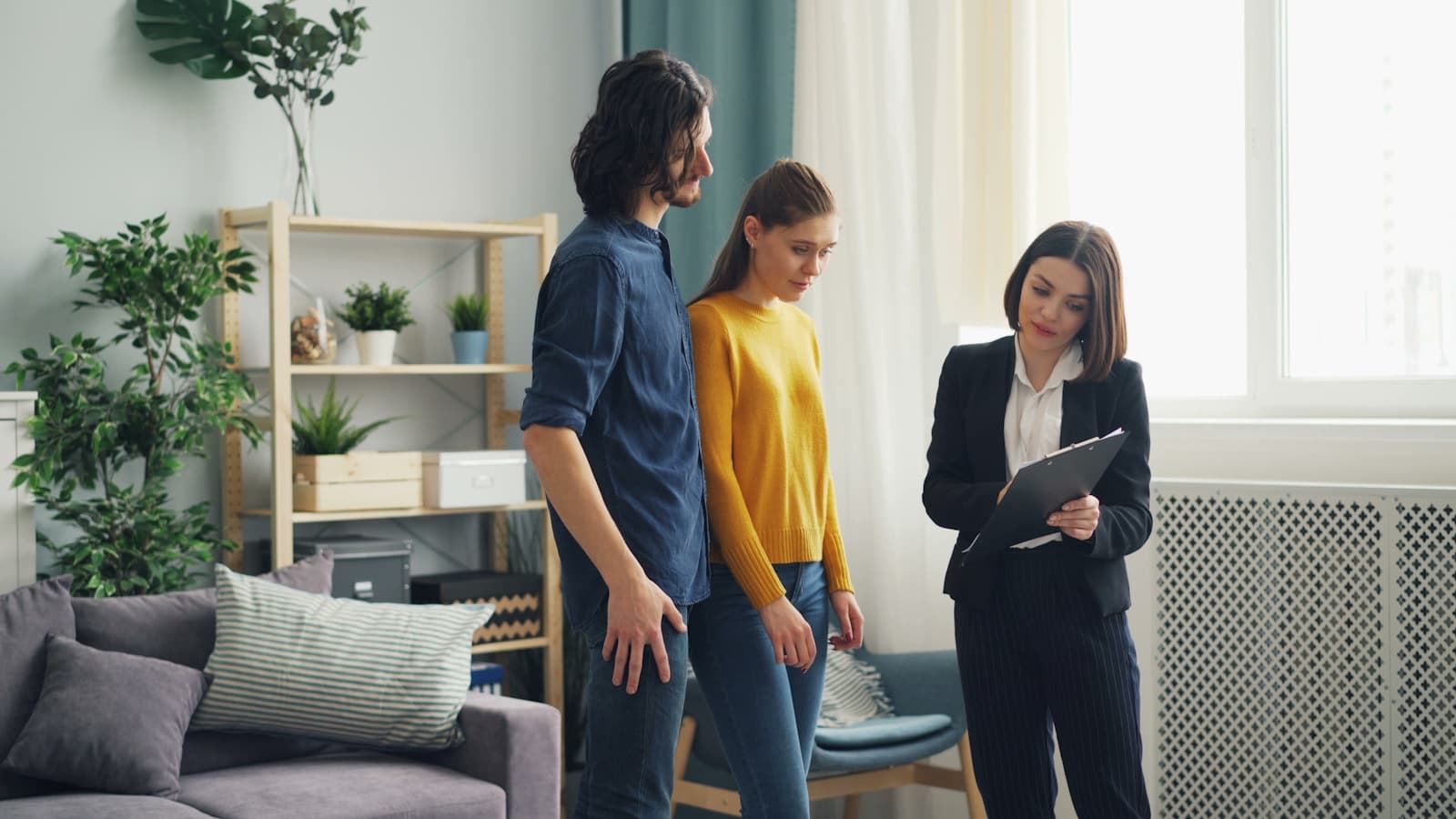 A professional with a clipboard talking to a couple in a living room.