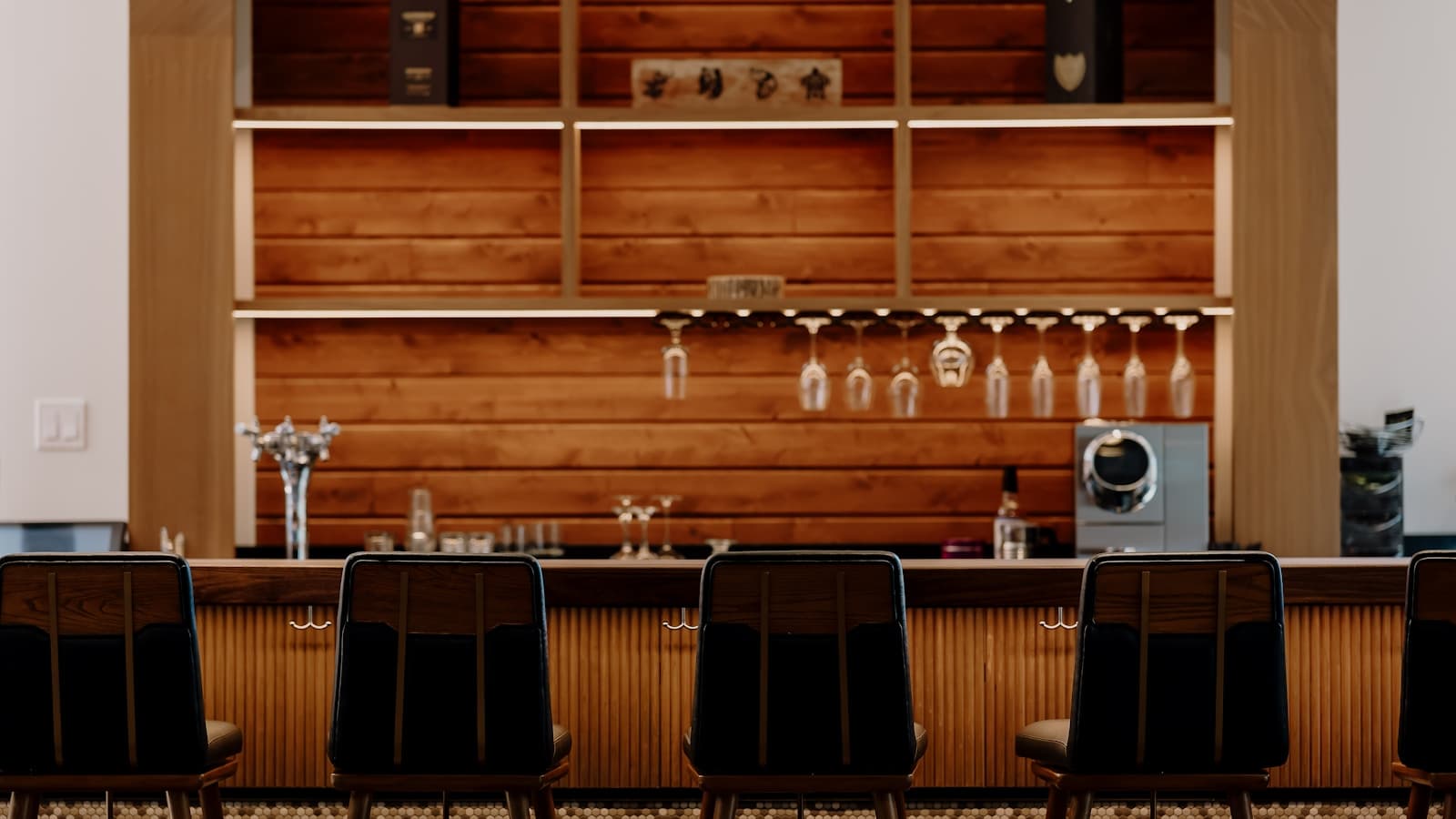 A modern bar counter with wooden accents and black stools, an upscale home-bar-style setup.
