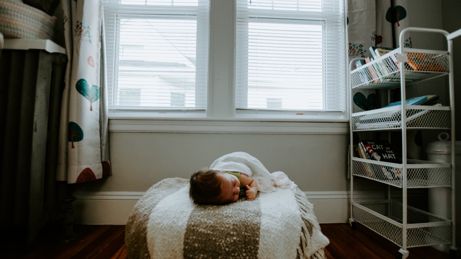 A newborn sleeping on a cozy blanket in a home bedroom by a window.