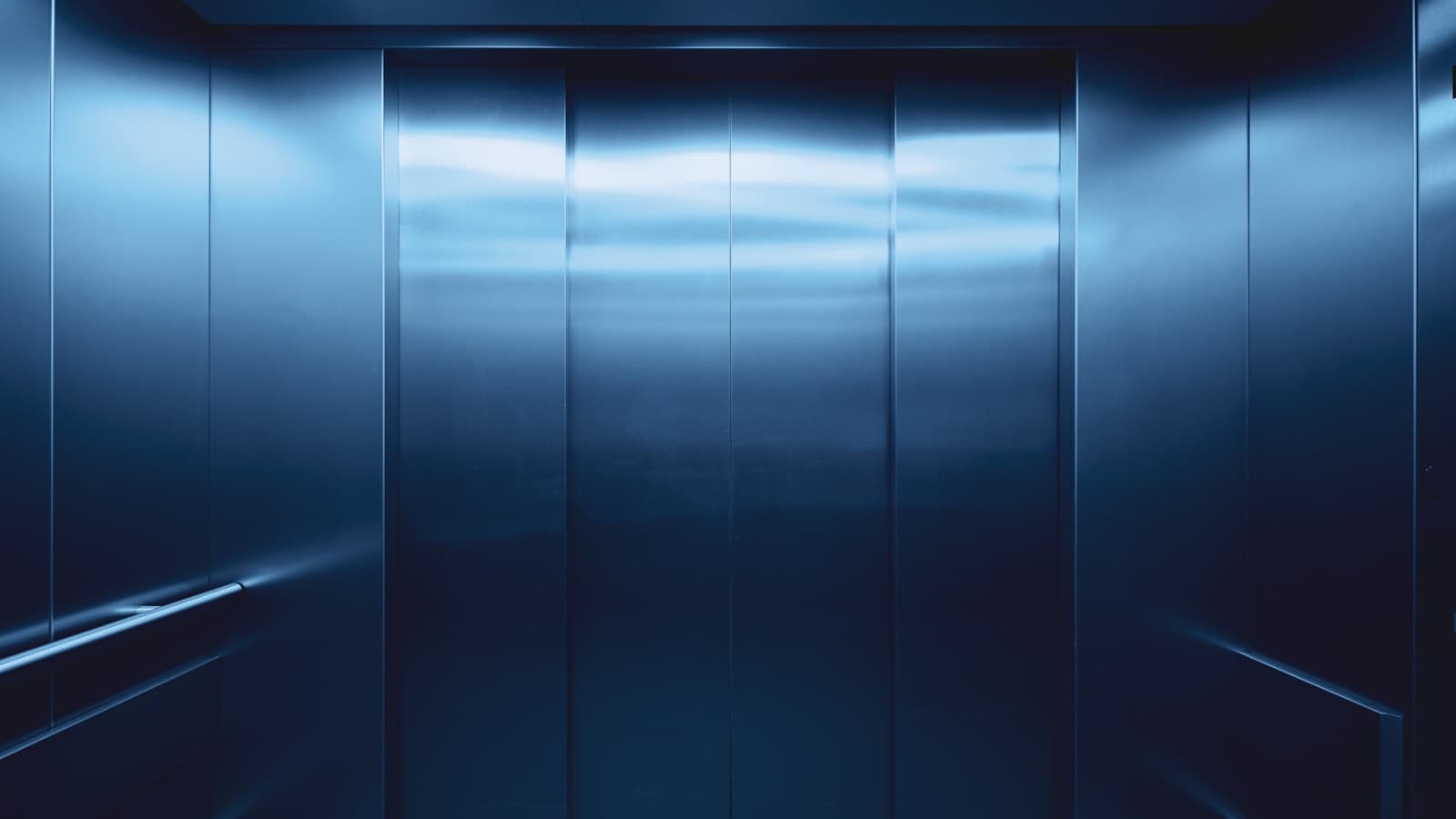 Clean interior view of a closed elevator car with brushed steel walls, no people, text, or logos.