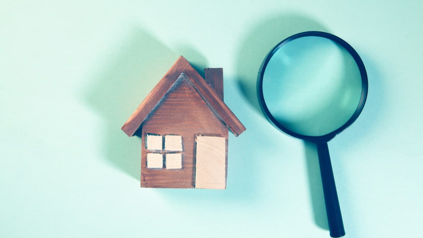 A magnifying glass held over a small wooden model house, symbolizing a home inspection.