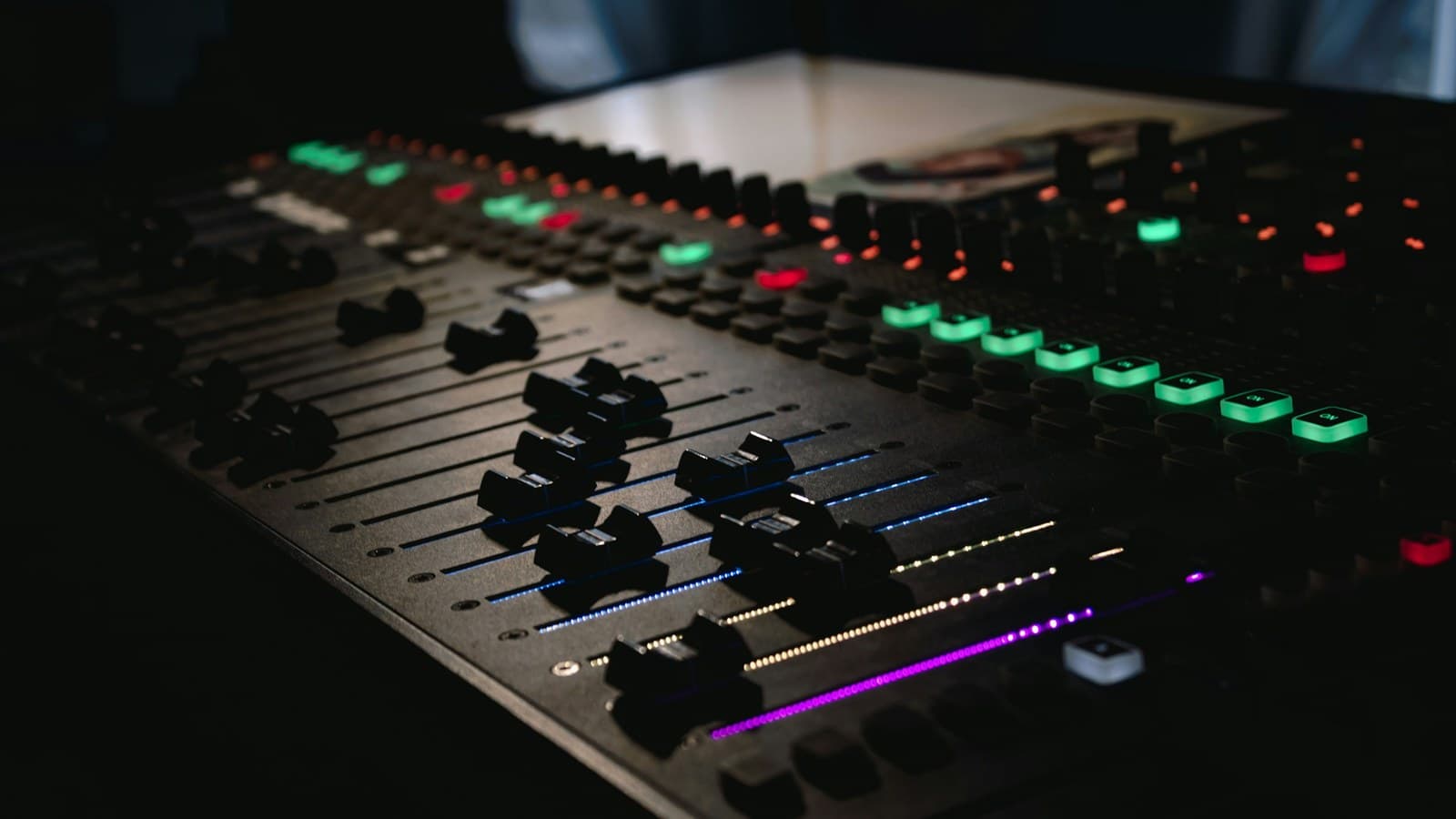 A close-up of an audio mixing console with illuminated buttons and knobs.