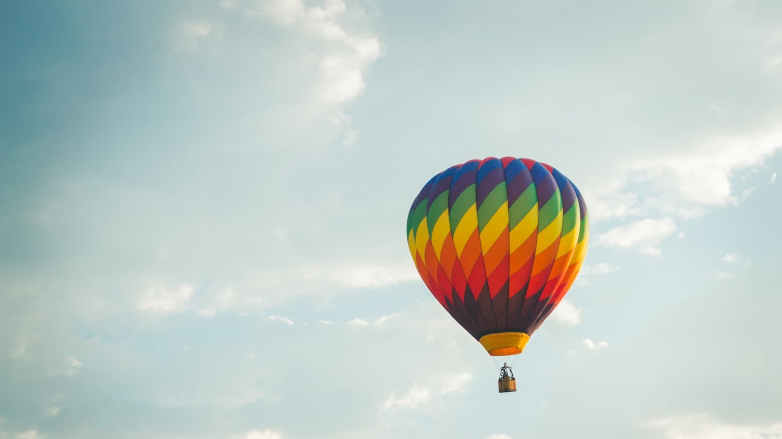 A single chevron-patterned rainbow balloon against a soft cloudy sky.