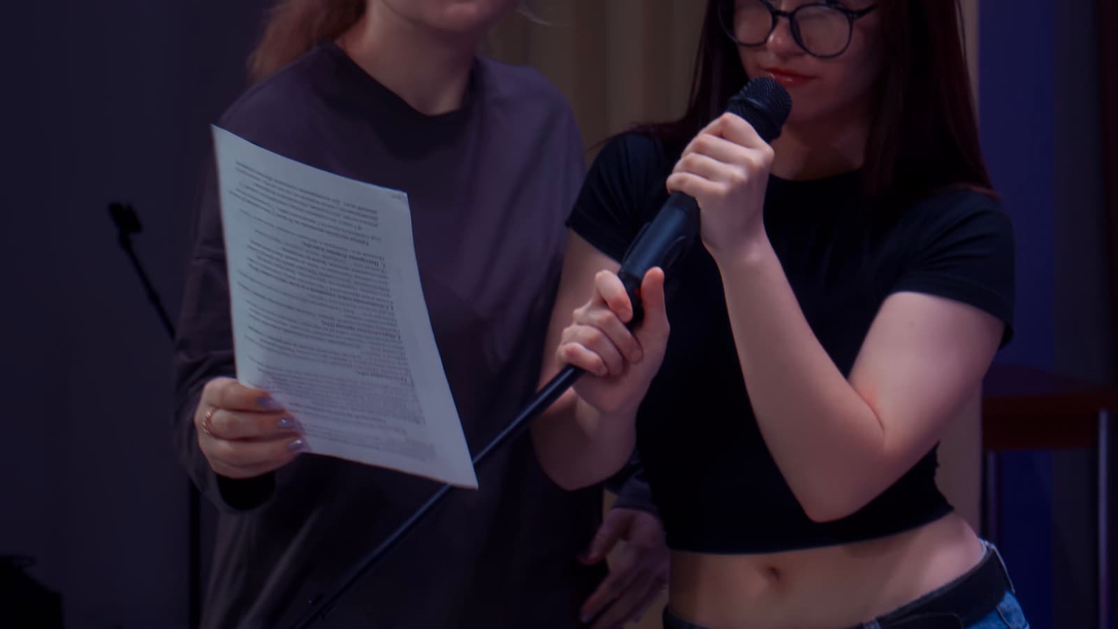 Two young women performing karaoke together with a microphone.