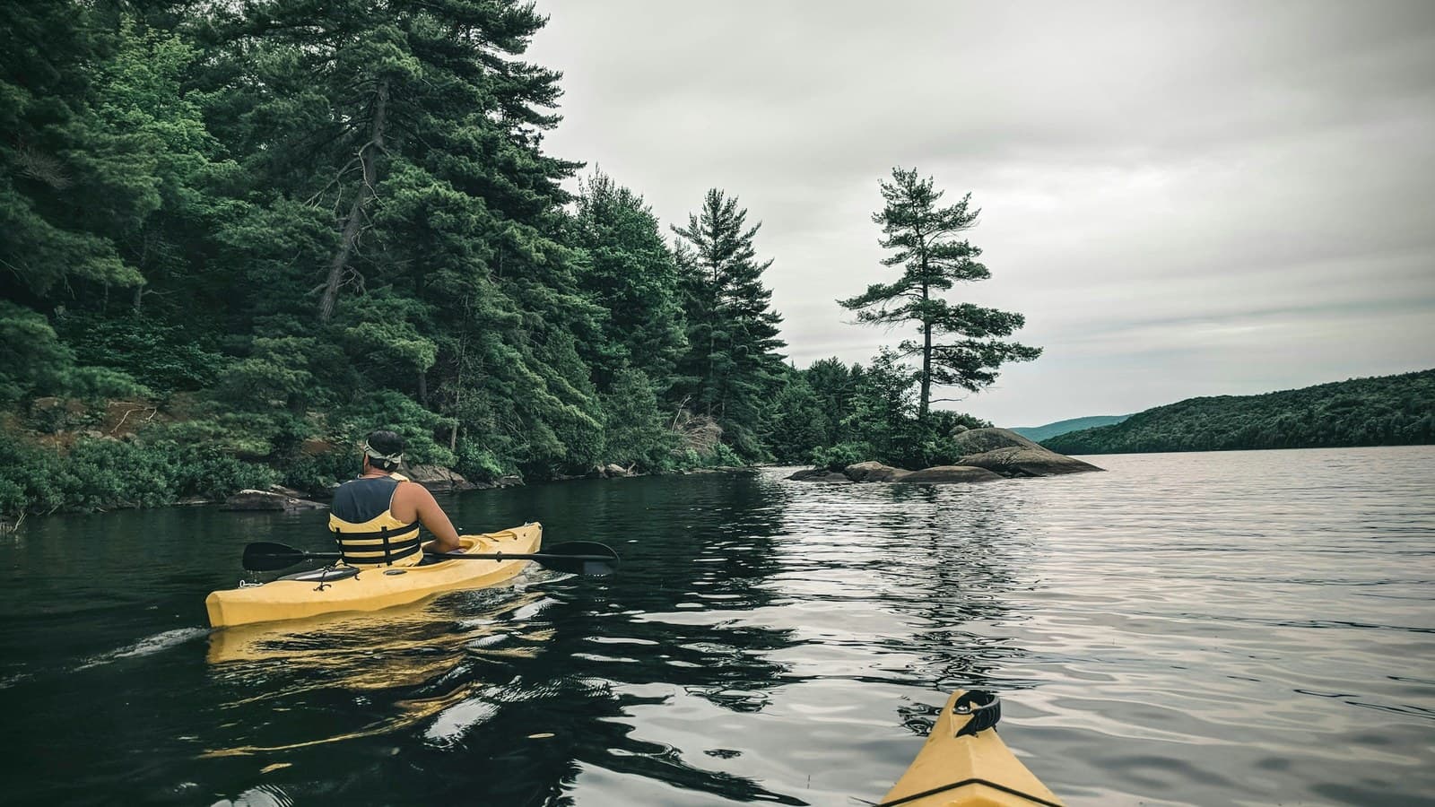 A person paddling a bright yellow kayak across a calm, forest-lined lake.