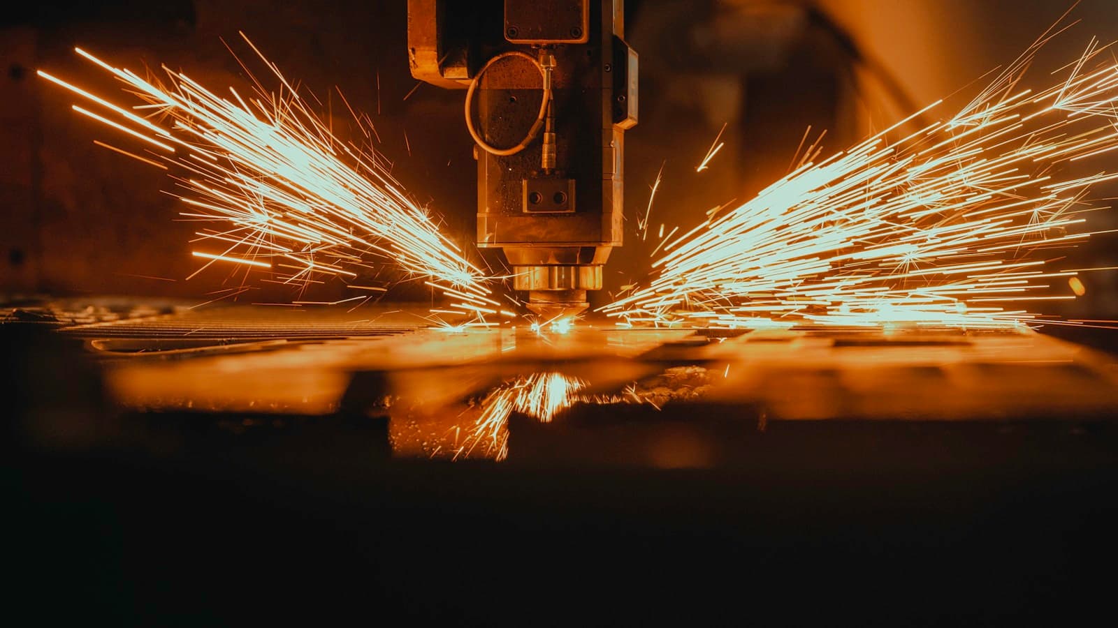 A laser cutting machine head throwing sparks while cutting through a piece of metal.