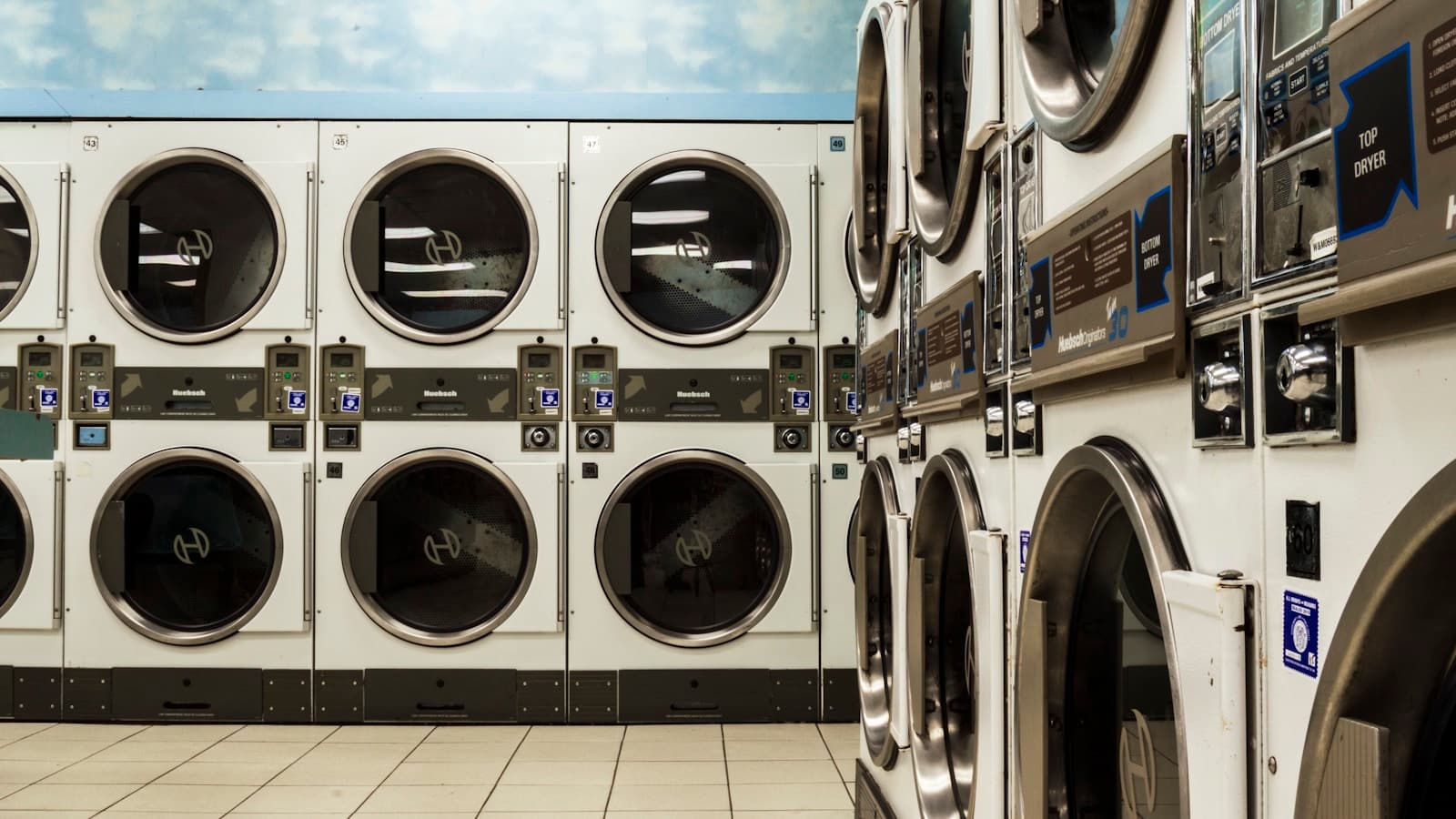 White washer and dryer units on a clean tiled laundromat floor.
