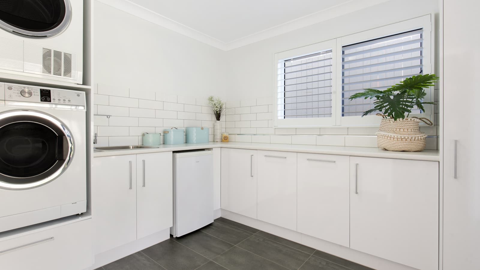 A bright, modern L-shaped laundry room with white cabinetry and dark tile floor.