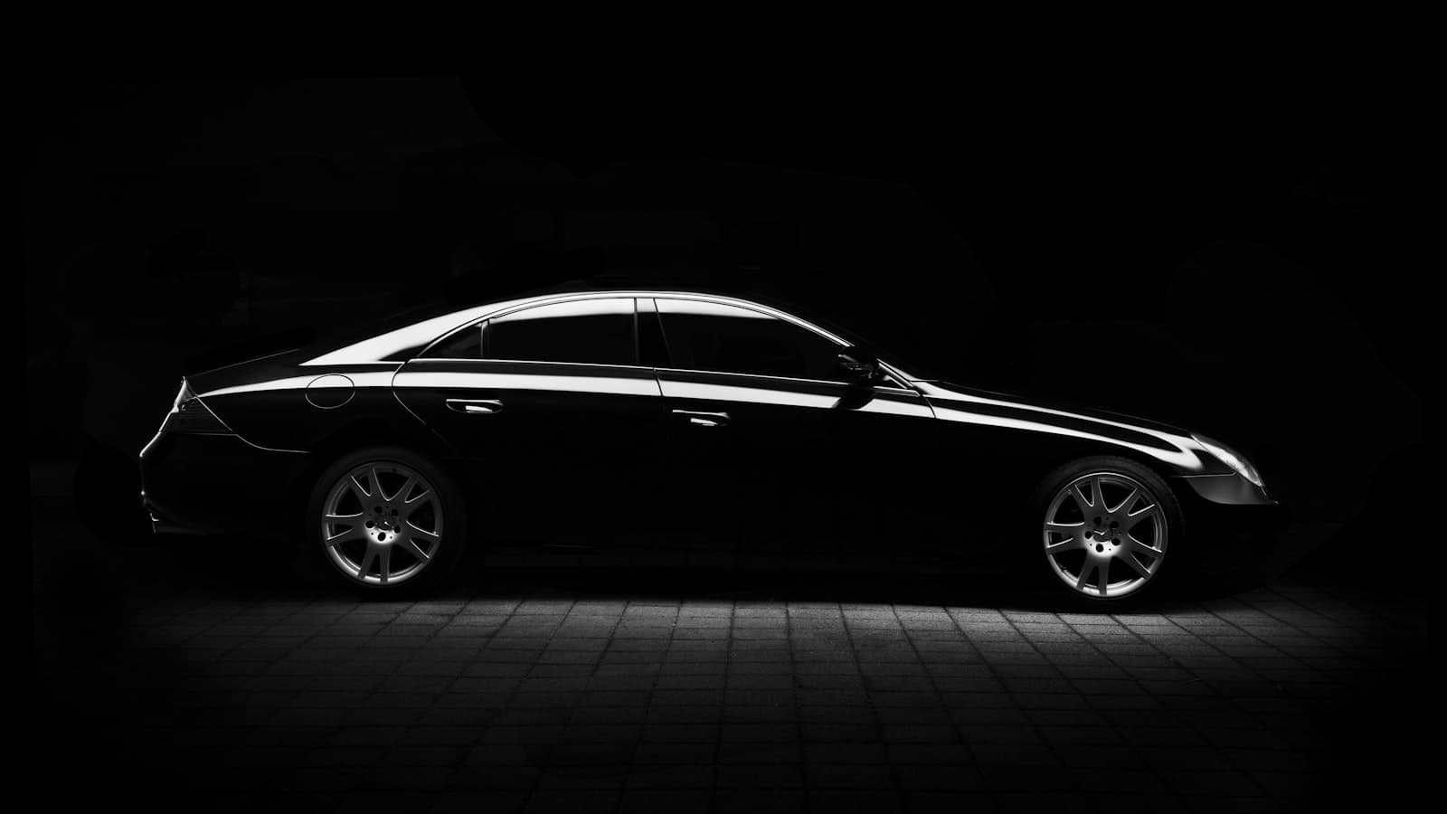 A sleek black luxury sedan photographed as a dramatic silhouette against a dark background, with no people, plate, or legible badge visible.