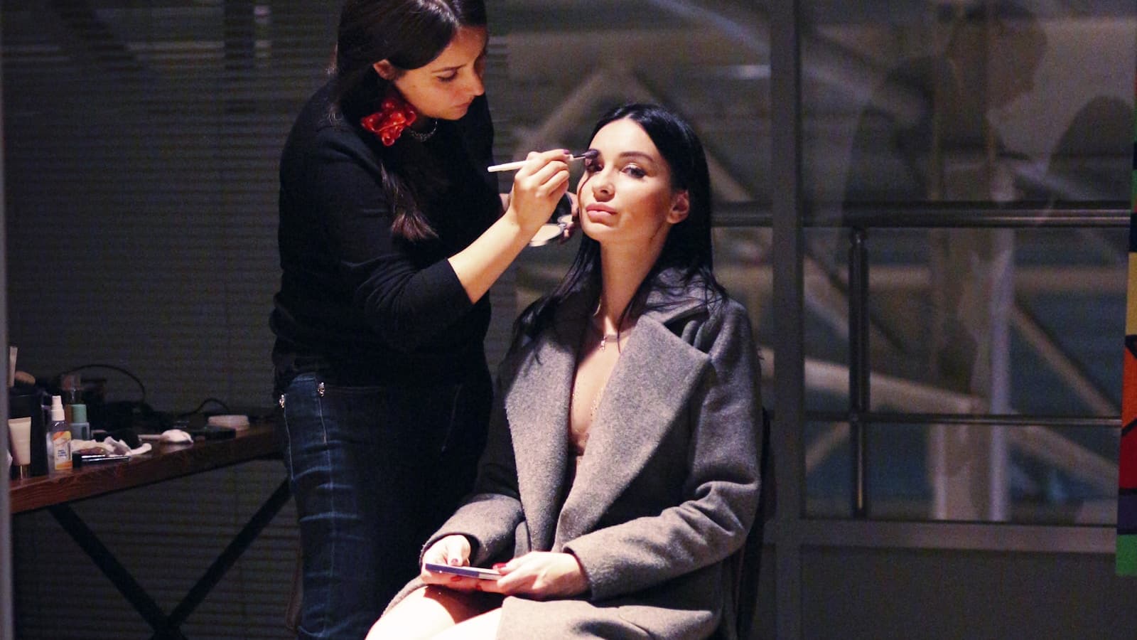 A makeup artist applying eye makeup to a seated client.