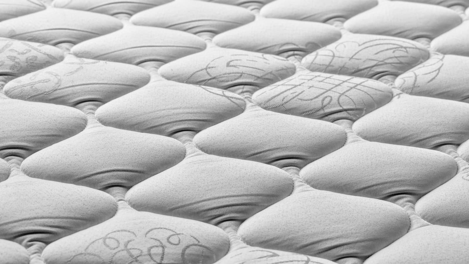 A close-up texture shot of a quilted white mattress surface, with no people, text, or logos visible.