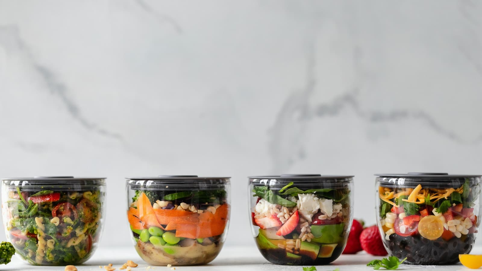 Four clear meal-prep containers with colorful salad and protein combinations.