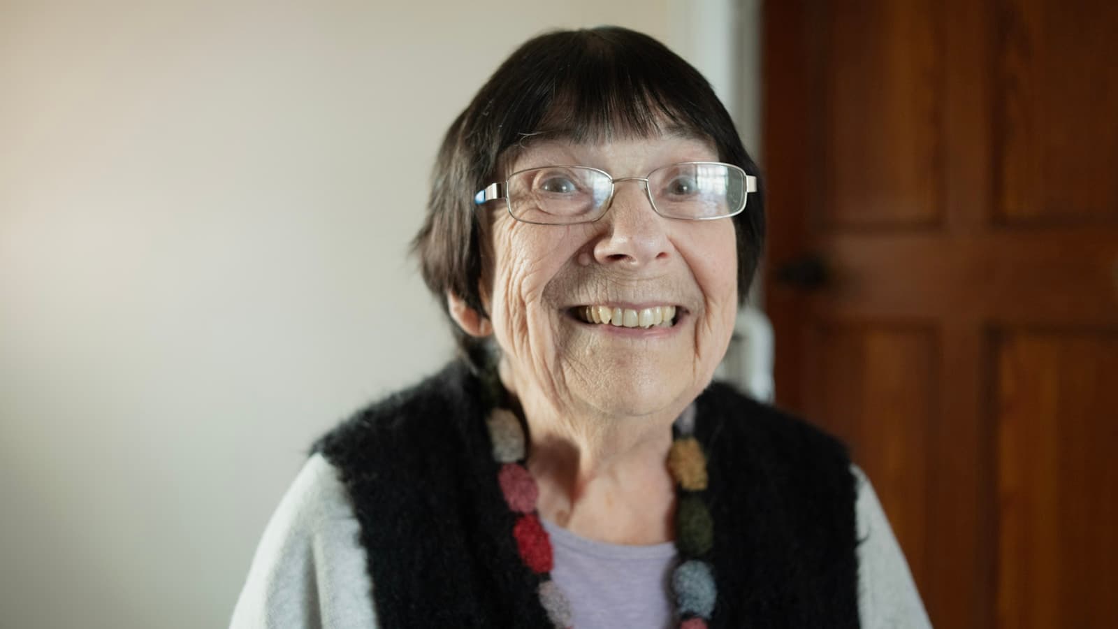 A smiling elderly woman wearing a simple pendant necklace.