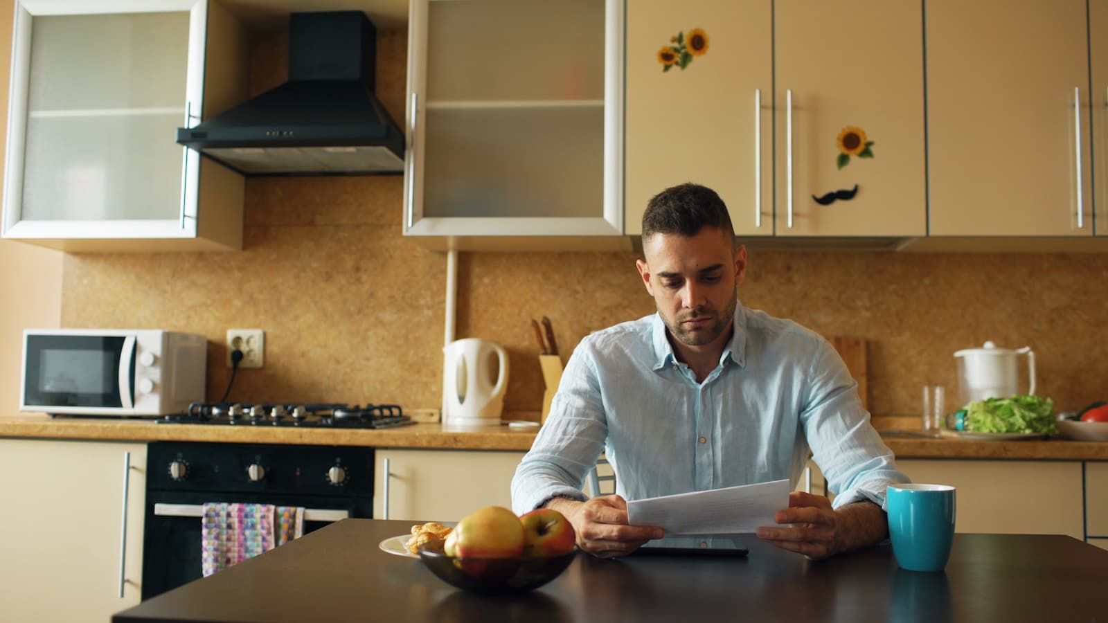 A man alone reading a bill at the kitchen table with coffee.