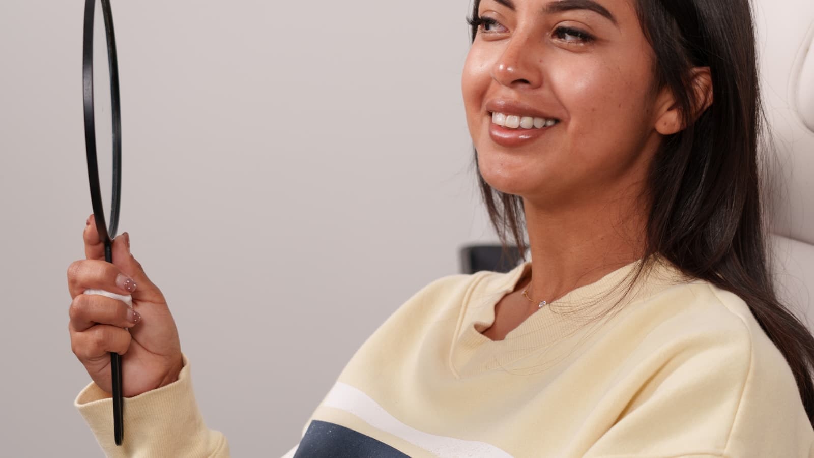A smiling patient in a clinic chair holding a mirror, happy and hopeful tone.